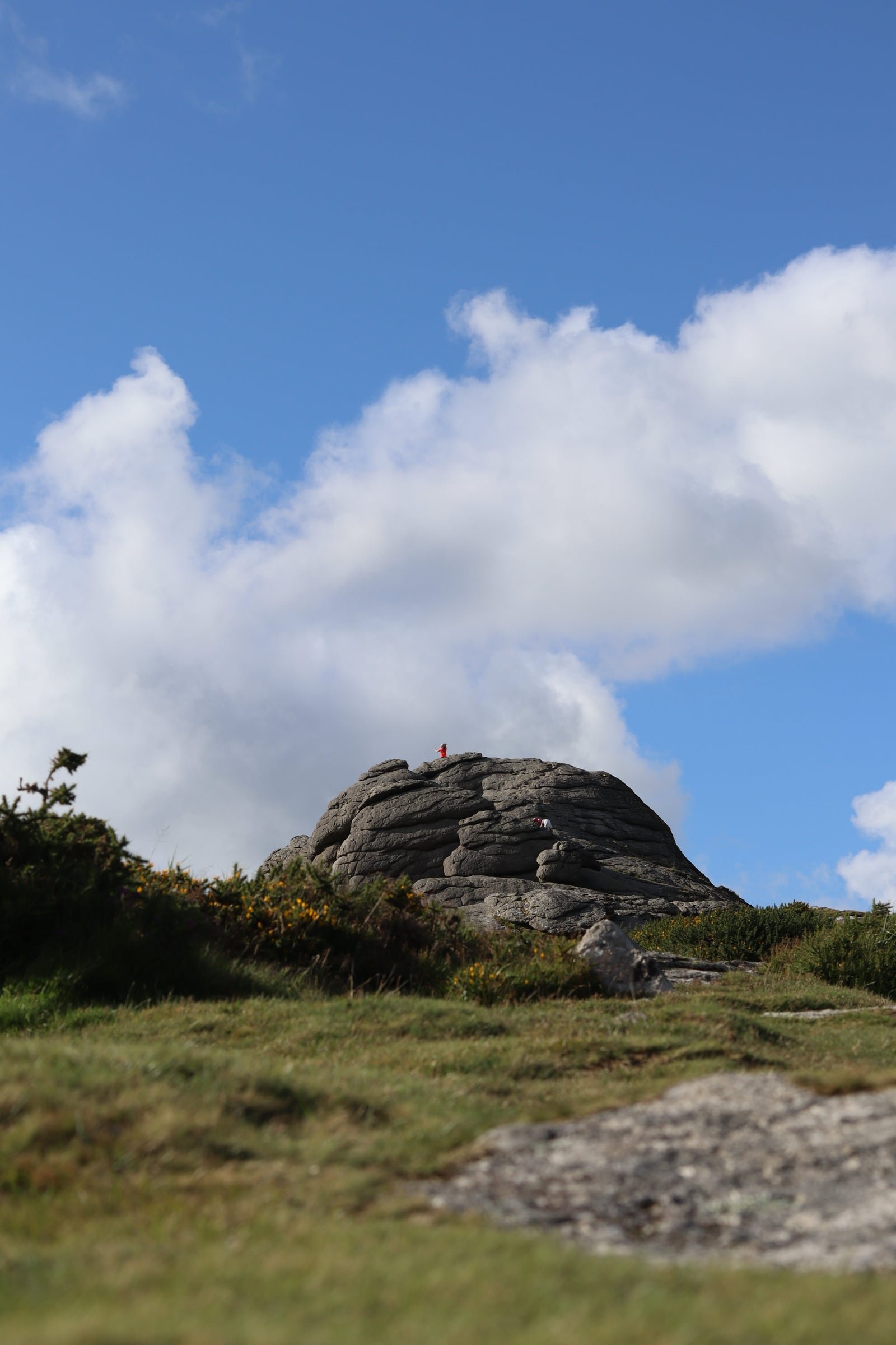 A granite tor on a grassy hillside under a blue sky and a bank of white cloud.