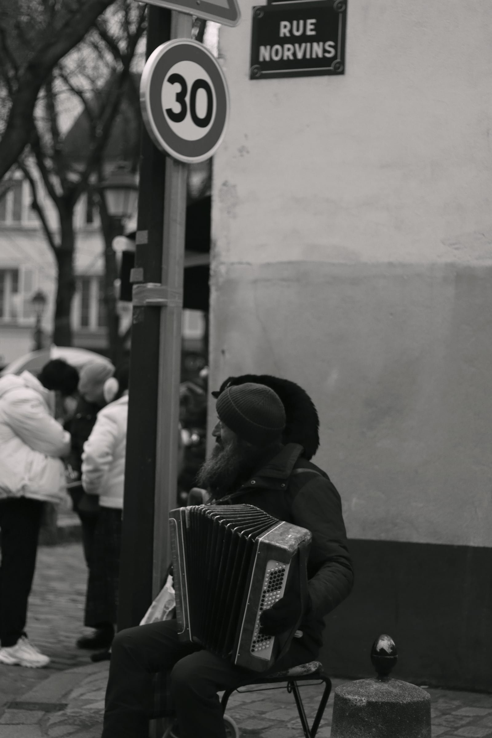 Black-and-white street scene: an accordion player seated at the corner of Rue Norvins in Montmartre.